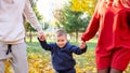 Mother and father lift up boy walking along autumn park