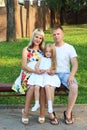 Mother, father, little daughter sit on bench in sunny p