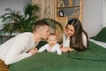 Mother and father are lying on the bed with their little son at home. Dad kisses his baby Royalty Free Stock Photo