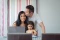 Mother and father make out with their baby girl painting on the notebook, with laptop computer in front, dining room table Royalty Free Stock Photo