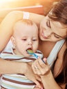 Mother feed her baby porridge by spoon outdoors in park.