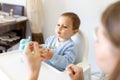 Mother feed little toddler baby boy with full mouth baby food, from plastic spoon in high chair view from back