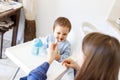 Mother feed little toddler baby boy with full mouth baby food, from plastic spoon in high chair view from back