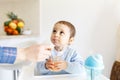 Mother feed little toddler baby boy with full mouth baby food, from plastic spoon in high chair view from back