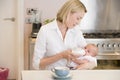 Mother feeding baby in kitchen with coffee Royalty Free Stock Photo