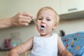 Mother feeding cute adorable caucasian little blond toddler boy with yogurt or milk cottage cheese for lunch snack Royalty Free Stock Photo