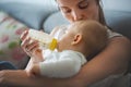 Mother, feeding her baby boy from bottle, sitting on the couch a Royalty Free Stock Photo