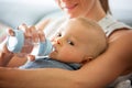 Mother, feeding her baby boy from bottle, sitting on the couch a Royalty Free Stock Photo