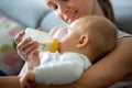 Mother, feeding her baby boy from bottle, sitting on the couch a Royalty Free Stock Photo