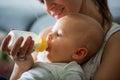 Mother, feeding her baby boy from bottle, sitting on the couch a Royalty Free Stock Photo