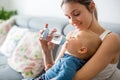 Mother, feeding her baby boy from bottle, sitting on the couch a Royalty Free Stock Photo