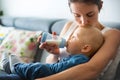 Mother, feeding her baby boy from bottle, sitting on the couch a Royalty Free Stock Photo