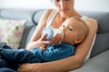 Mother, feeding her baby boy from bottle, sitting on the couch a Royalty Free Stock Photo