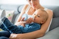 Mother, feeding her baby boy from bottle, sitting on the couch at home Royalty Free Stock Photo