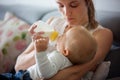 Mother, feeding her baby boy from bottle, sitting on the couch a Royalty Free Stock Photo