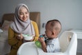 Mother feeding her baby boy while sitting on high chair Royalty Free Stock Photo