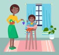 Mother feeding her baby child sitting on kids eating chair. Black woman holding fruit gives the baby Royalty Free Stock Photo