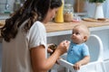 Mother feeding her baby son or daughter with spoon. Mother giving healthy food to her adorable child at home. Lovely mommy and her Royalty Free Stock Photo