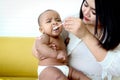 Mother feeding her cute little girl Asian African American baby daughter with spoon of food, infant kid enjoy eating healthy Royalty Free Stock Photo