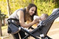 Mother feeding her son with a milk bottle in the park inside the baby stroller