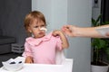 Mother feeds the baby girl with a spoon. The two-year-old child is naughty and refuses to eat. Cute baby grimaces because he does Royalty Free Stock Photo