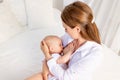 Mother feeds baby 6 months of breast sitting on a white bed at home, place for text Royalty Free Stock Photo