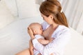 Mother feeds baby 6 months of breast sitting on a white bed at home, place for text Royalty Free Stock Photo
