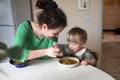 Mother feeds the child soup in the bright kitchen at home