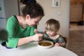 Mother feeds the child soup in the bright kitchen at home