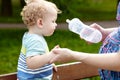 Mother feeds her baby from bottle with water in city park Royalty Free Stock Photo