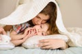 Mother gently kisses her son on cheek. they are lying on bed covered with bedspread in bright bedroom. She hugs child Royalty Free Stock Photo