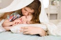 Mother gently kisses her son on cheek. they are lying on bed covered with bedspread in bright bedroom. She hugs child Royalty Free Stock Photo