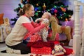 Mother gets the baby out of the gift box on background of the Christmas tree and lights