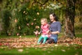 Mother and girl having fun under tree with autumn leaves in the park, blond cute curly girl, happy and young family Royalty Free Stock Photo