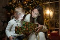 Mother gives her little son a Christmas gift box. Little son opens a gift box on the background of a Christmas tree Royalty Free Stock Photo