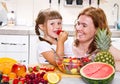 A mother gives to the little girl a fruit salad in the kitchen.