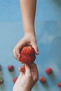 Mother giving her son a big red strawberry. Little boy taking a strawberry from mom`s hand. Little strawberries on bright blue Royalty Free Stock Photo