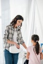 mother in grey shirt pouring liquid laundry detergent in washer wile daughter in pink t-shirt standing near