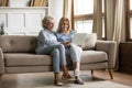 Mother and grownup daughter sitting on couch using computer