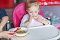 Mother hand feeding infant girl with spoon in high baby chair in kitchen at home Royalty Free Stock Photo