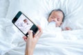 Mother hand hold mobile phone to take a photo of newborn baby during she is sleeping on white bed Royalty Free Stock Photo