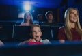 Mother with happy small children in the cinema, watching film.