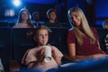 Mother with happy small children in the cinema, watching film and drinking with a straw.