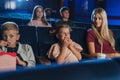 Mother with happy small children in the cinema, watching film.