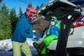 Mother help young boy to put on snowboard boots at car parking Royalty Free Stock Photo