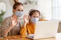 Mother helping daughter with remote education and greeting teacher during online lesson during pandemic