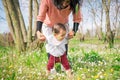 a mother helping her baby daughter move the first steps in a meadow in the countryside outdoors. Toddler making her first steps