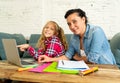 Mother helping young girl doing homework with laptop and school books sitting on the sofa at home in parenting homework and Royalty Free Stock Photo