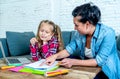 Mother helping young girl doing homework with laptop and school books sitting on the sofa at home in parenting homework and Royalty Free Stock Photo