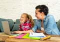 Mother helping young girl doing homework with laptop and school books sitting on the sofa at home in parenting homework and Royalty Free Stock Photo